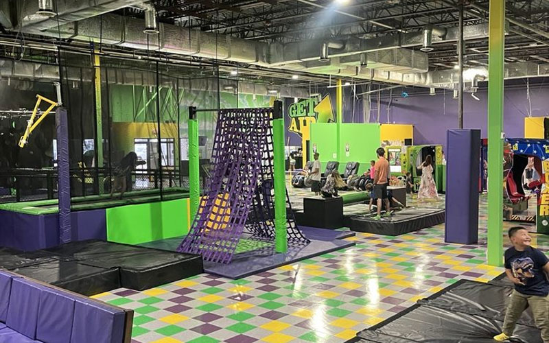 Indoor obstacle game area with trampoline-integrated hurdles, climbing walls, and balance challenges