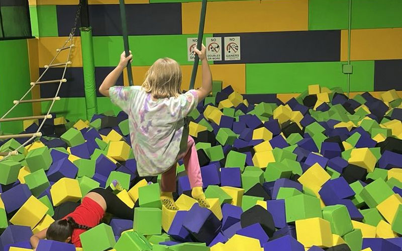 Trampoline foam pit with deep safety foam and a clear net enclosure in a busy indoor trampoline park