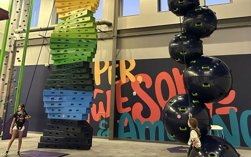 Indoor climbing wall with varying difficulty levels and safety harnesses in a family-friendly shopping center