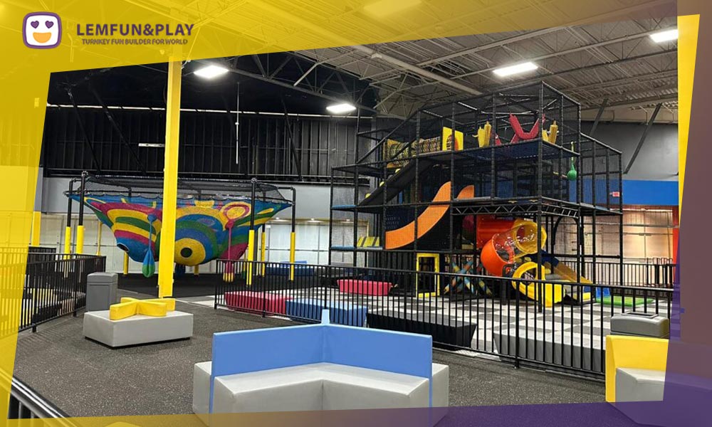 A panoramic aerial view of a complete commercial indoor playground facility, showcasing the 60/40 design split between play equipment and revenue-generating cafe/party zones.