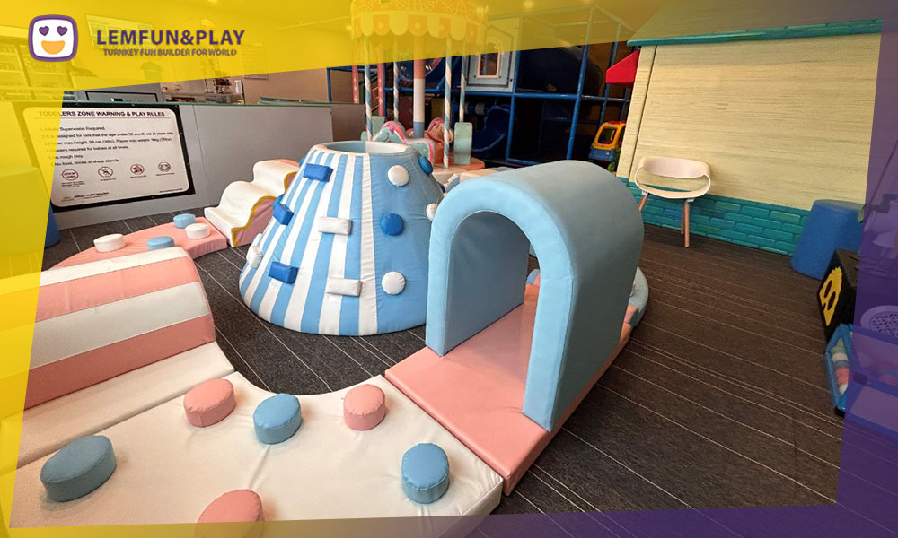 Toddler-safe soft play area with macaron-shaped foam climbing blocks and licorice-themed tunnels in a candy theme.