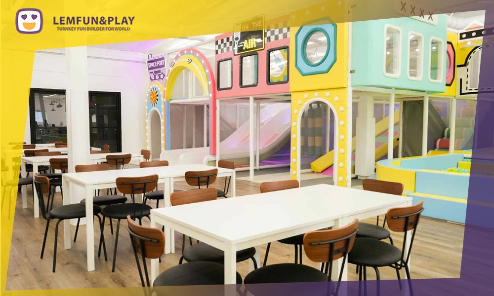 Integrated dining and cafe area within an indoor playground, showing parent seating with a clear view of the play zones.