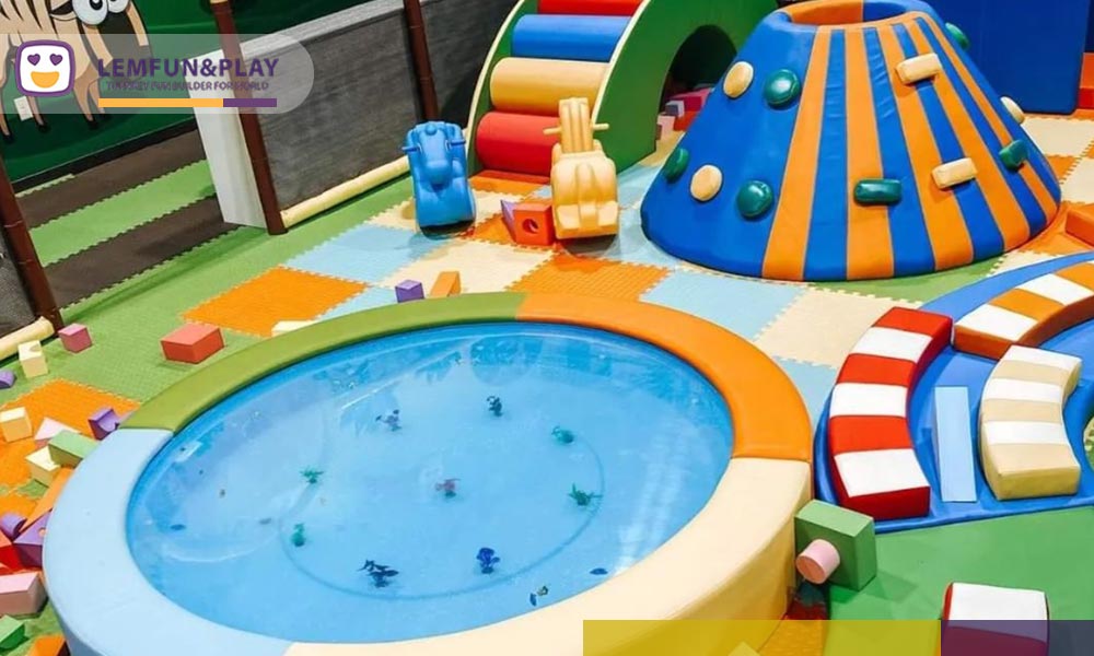 An intimate photograph focusing on the enclosed kids' soft play area, featuring soft foam jungle animals, oversized soft building blocks, and a small ball pit where a toddler is crawling, surrounded by safety padding.