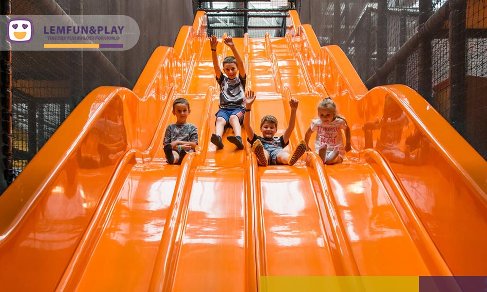 Vibrant four-lane orange wave slide integrated into a large scaled indoor playground set for kids and teenagers.