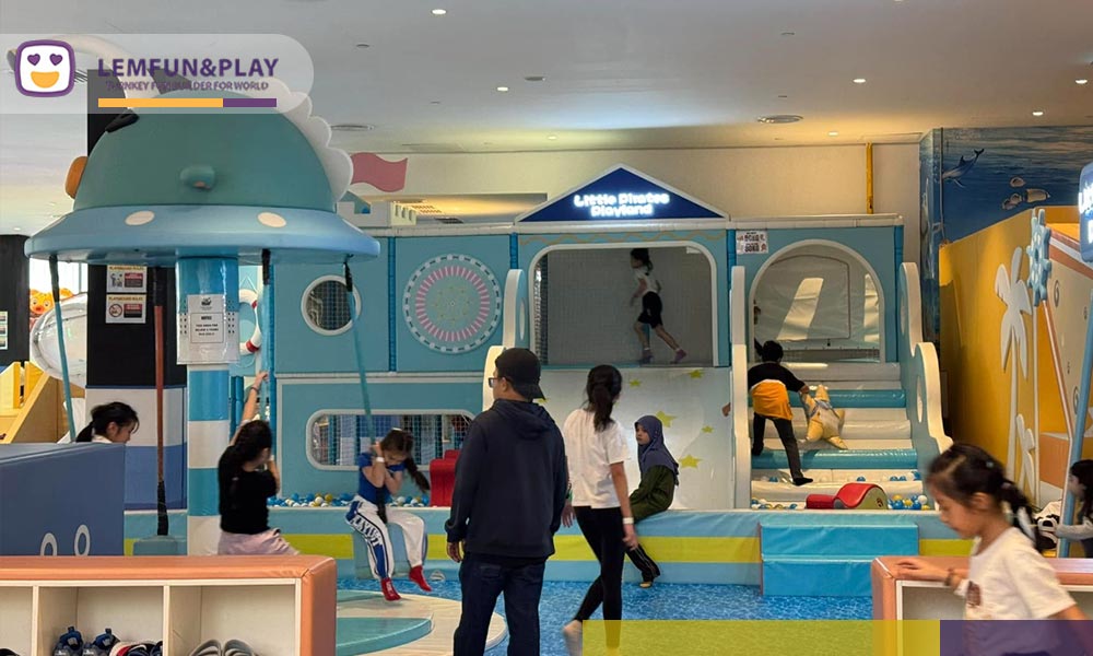 Motorized blue-and-white striped spinning mushroom carousel installed over water-ripple safety flooring in a macaroon themed soft play zone.