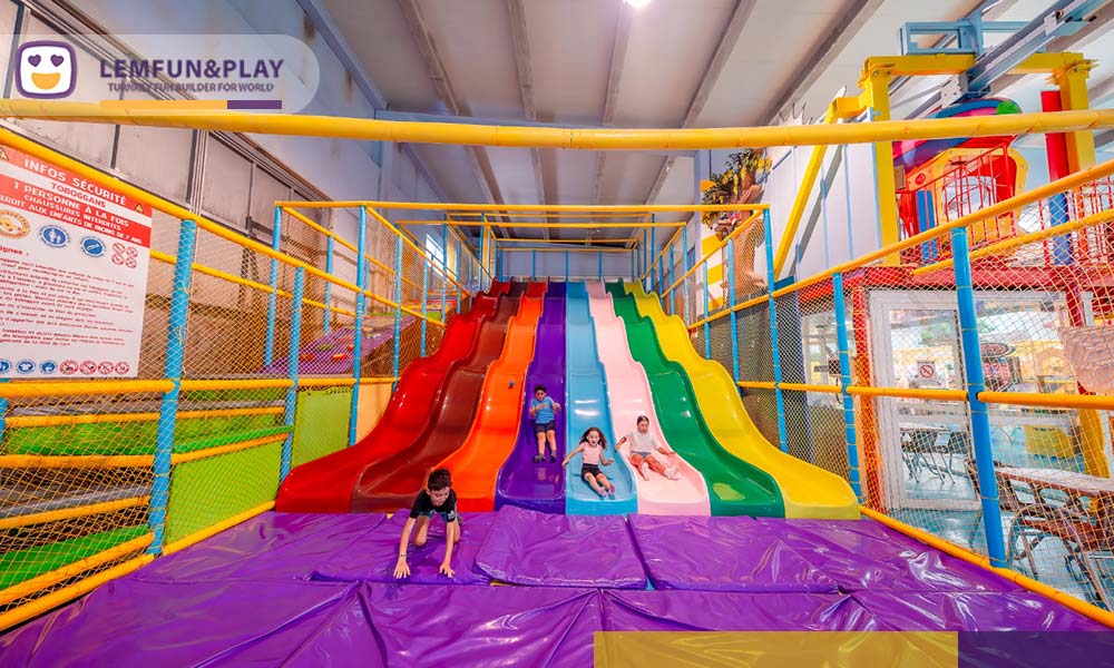 Vibrant 6-lane rainbow wave slide with protective landing pads at Europark Indoor in Vias, France.